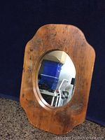 Front view of the rustic wooden frame mirror showing oval glass and wood grain with wear marks.