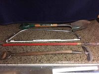 Full set of four garden tools including shovel, edger, planting shovel, and saw laid out on a flat surface.