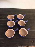 Six Le Creuset French Onion Soup Bowls arranged on a dark wooden surface, showing handles and interior.