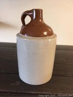 Front view of vintage stoneware jug showing beige stoneware body and brown glazed top with handle.