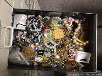 Drawer filled with assorted vintage costume jewelry including necklaces, pendants, earrings, and pins piled together.