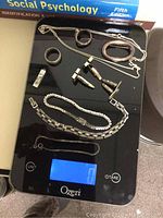 Top view showing rings, cufflinks, bracelets, pendant, and chain necklace on scale.