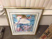 Framed lithograph of a cockatoo with pink crest, in gold metal frame on floor.