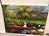Framed oil on canvas painting showing a scenic river setting with people in boats and a background of trees and buildings