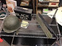 Top view of helmet, machete with sheath, and ammunition box on wire rack