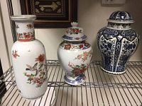 Photo of three vases including a tall white vase with floral and bird designs, a covered urn with floral patterns, and a blue and white Delft-style urn with lid and chip on rim.