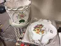 Decorative porcelain planter with scalloped edges and floral designs alongside a floral serving platter and smaller dish.