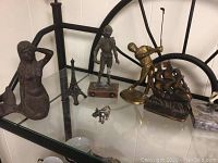 Photo of decorative statues including brass or bronze figures, plastic knight on marble base, Eiffel Tower, mermaid, and small elephant.