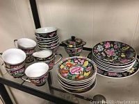 Photo of 5 floral teacups, 6 matching saucers, a floral pattern teapot, and assorted plates with a black floral background.