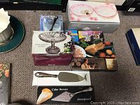 Assortment of boxed glassware and utensils including cake servers with visible box wear