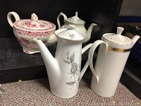Photo showing all four porcelain tea pots grouped together on a counter with black background. Various designs seen including floral and gold accents.