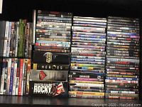 Photo showing stacked DVDs including Rocky Anthology, Star Wars Trilogy, Heroes, Superman, Inception, Cowboys & Aliens. Various other titles also seen.
