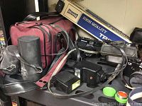 Overview of vintage cameras, flashes, carrying bags, and boxed tripod showing lot contents.