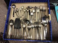 Top view of various silver plated flatware including spoons, forks, knives, serving pieces in blue box.
