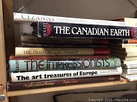 Stack of art books focusing on artists including Cézanne, The Canadian Earth, The Prado Madrid, Impressionists, and European art treasures.