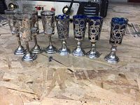 Full front view of all 8 shot glasses arranged in one line on a plywood board surface showing both clear and blue glass types with silver holders.