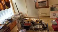 Overview of assorted hand tools, painting supplies, and boxes near a window and air conditioning unit