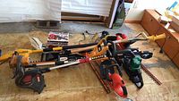 Photo showing laid out garden power tools including chainsaw, hedge trimmers, weed eaters and weed whackers on floor