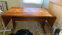 Full view of wooden drop side trestle table with inlaid decorative tiles, showing closed sides and tile details.