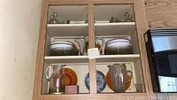 Cabinet shelf with stacked amber glass plates, fruit-themed orange glass plates, clear pitchers, and salad dressing bottles.