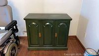 Front view of the green rolling liquor cabinet bar showing three arched doors and base.