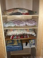Sealed bags of assorted bedding stacked on shelves in a wooden shelving unit.
