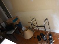 Photo showing metal walker, blue seat stool, black lanterns, and lampshade on floor