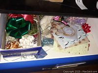 Photo of assorted gift bows in colors red, green, white, gold, and silver along with gift wrapping paper and some small packages.