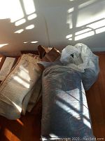 Folded fabric pieces with cream background and brown stripes, partially wrapped in bags and loose on floor under sunlight.