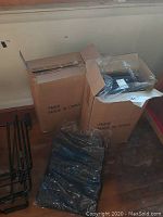 Boxes containing blue luggage pieces and packaged luggage piece on floor with black luggage cart frame beside them.