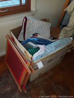 Box of multiple handmade quilts and quilting accessories including wooden frames packed inside a cardboard box placed beside a window.