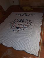 Full view of largest handmade quilt showing white background with heart and leaf appliqué, scalloped edges on wooden floor