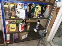 Wide shot of metal garage shelving containing various cleaning and waxing products including spray bottles, cans and a small box.
