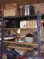 Shelving with multiple kitchen items including stock pots, roasting pans, jars, mixing bowl, rolling pin, brass cup, and packaged Wonder Baker