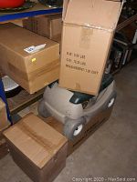 Wheeled gardening seat with boxes stacked on it and nearby in a garage setting