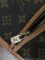 Close-up of monogram canvas and zipper pull stamped with LV logo