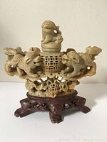 Front view of the antique hand-carved stone figure with wooden base, showing two lion figures and central lattice sphere with a smaller lion on top.