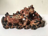 Front view of the hand carved stone sculpture with reddish and black coloration.