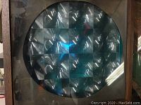 Close-up photo of the front of the vintage color organ motion light showing the circular multi-faceted lens reflecting blue light inside a wooden square frame.