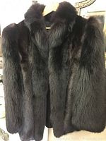 Front view of black mink coat hanging on wooden hanger