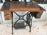 Full view of wooden sewing machine cabinet with cast iron treadle base and two small drawers on each side.