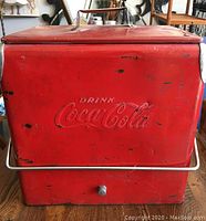 Front view of red Coca-Cola cooler showing embossed logo, chrome handle and drain plug