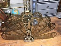 Full view of the vintage brass folding fireplace screen showing its fan shape and decorative elements.