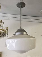 Full view of the pendant light fixture showing the white glass shade and metal support rod and mounting plate at the ceiling.