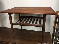 Frontal view of side table showing rectangular top, tapered legs and slatted shelf