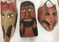 Three vintage hand-carved wooden masks laid out on a white surface, showing distinct facial and animal features with painted details.