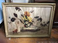 Front view of vintage floral print in ornate gold frame resting on floor.