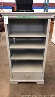 Full front view of gray shelving unit showing four shelves and bottom drawer with white knob.