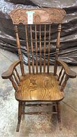 Front view of wooden rocking chair showing carved top backrest and vertical spindles.