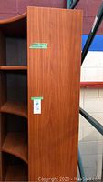 Left side profile view of wood-tone corner shelving unit showing five curved shelves and tall height.